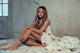Carly Pearce wearing a white dress in an empty room sitting on a painter's tarp in front of a washed white wall.